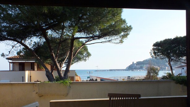 Una mesa y sillas de madera en un balcón con vistas a la costa, árboles y edificios.