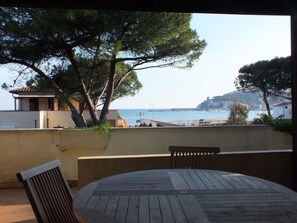A wooden table and chairs on a balcony overlooking a coastal view with trees and buildings.