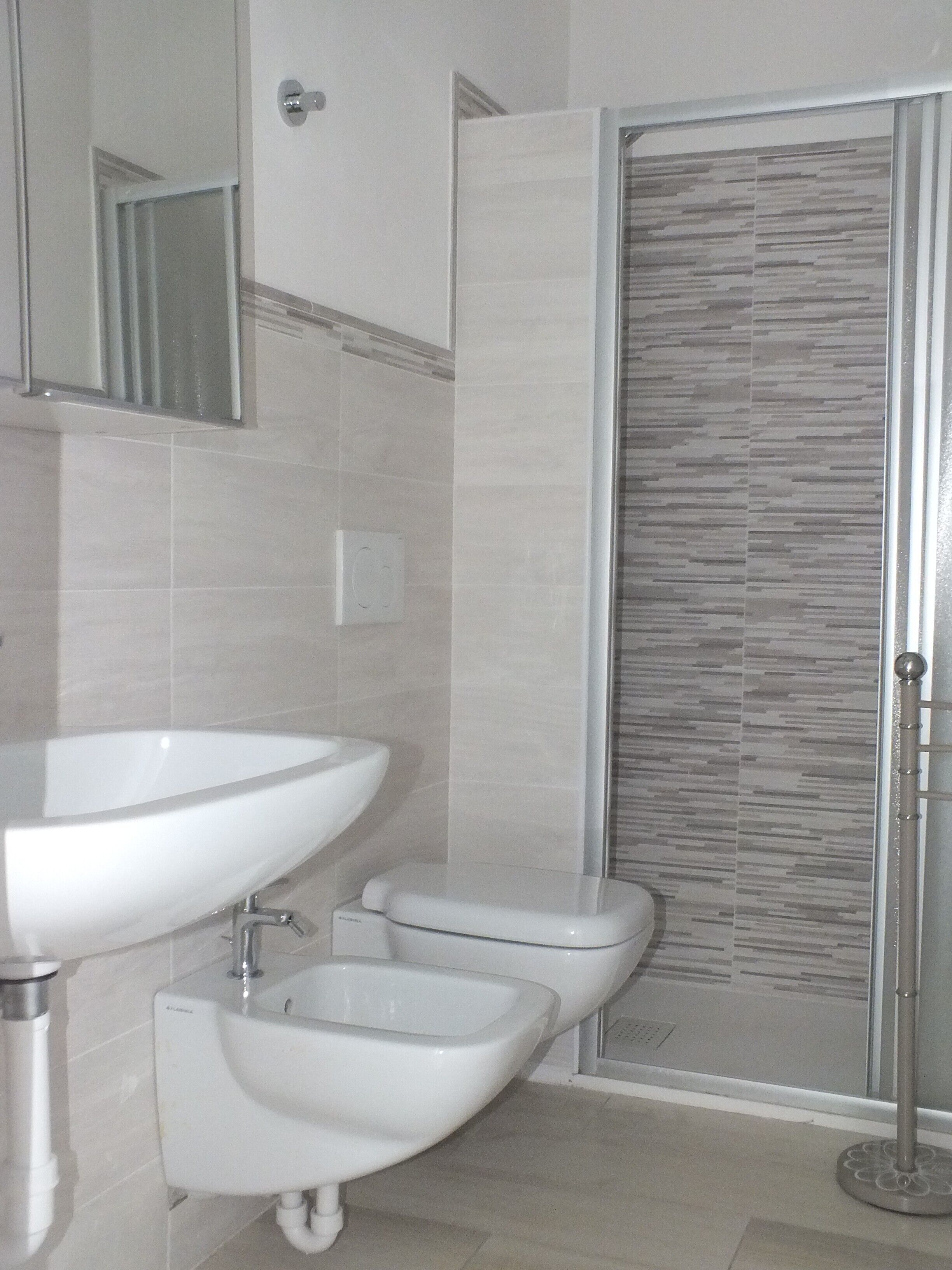 Een badkamer met een wastafel, toilet, bidet en een douche met een deur met een patroon.
