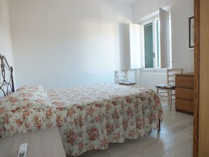 A bedroom with a bed, a wooden dresser, a chair, and a window with blinds.