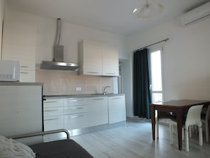Een moderne keuken met witte kasten, een magnetron en een eethoek met een tafel en stoelen.