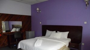 A hotel room with a large bed, a desk, a chair, a mirror, and a nightstand. - Belden s Nest Lodge (Ndola)