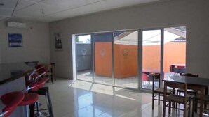 A spacious room with a large sliding glass door leading to an outdoor area with a table and chairs. - Belden s Nest Lodge (Ndola)