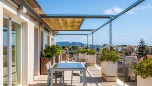 A rooftop terrace with a table and chairs, potted plants, and a view of the cityscape. - Amazing penthouse with stunning views of the sea and the mountains. (Cala Millor)