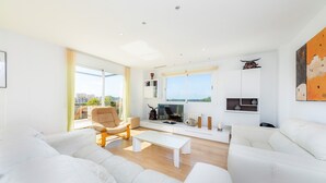A modern living room with a sofa, armchair, coffee table, TV, and a view of the city. - Amazing penthouse with stunning views of the sea and the mountains. (Cala Millor)