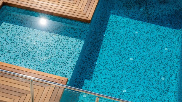 A swimming pool with a tiled floor and wooden deck area. - Amazing penthouse with stunning views of the sea and the mountains. (Cala Millor)