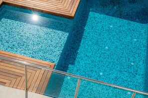 A swimming pool with a tiled floor and wooden deck area.