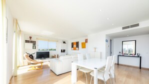 A modern living room with a white sofa, a dining table with chairs, a TV, and artwork on the walls. - Amazing penthouse with stunning views of the sea and the mountains. (Cala Millor)