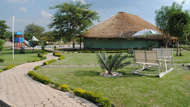 Un parque con una estructura de techo de paja, un parque infantil y un camino pavimentado.
