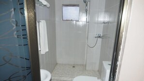 Un baño con inodoro, ducha y una ventana pequeña.