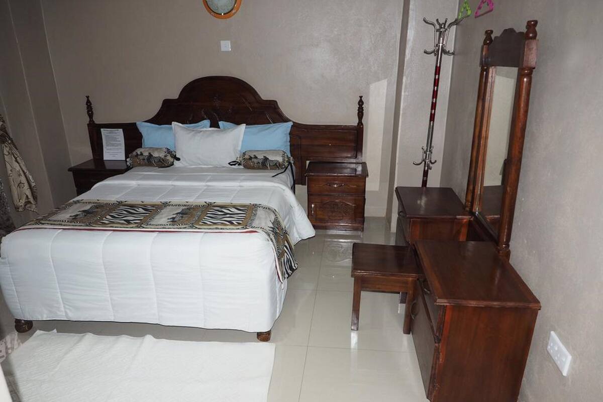 A bedroom with a large bed, a wooden dresser, a mirror, and a nightstand.