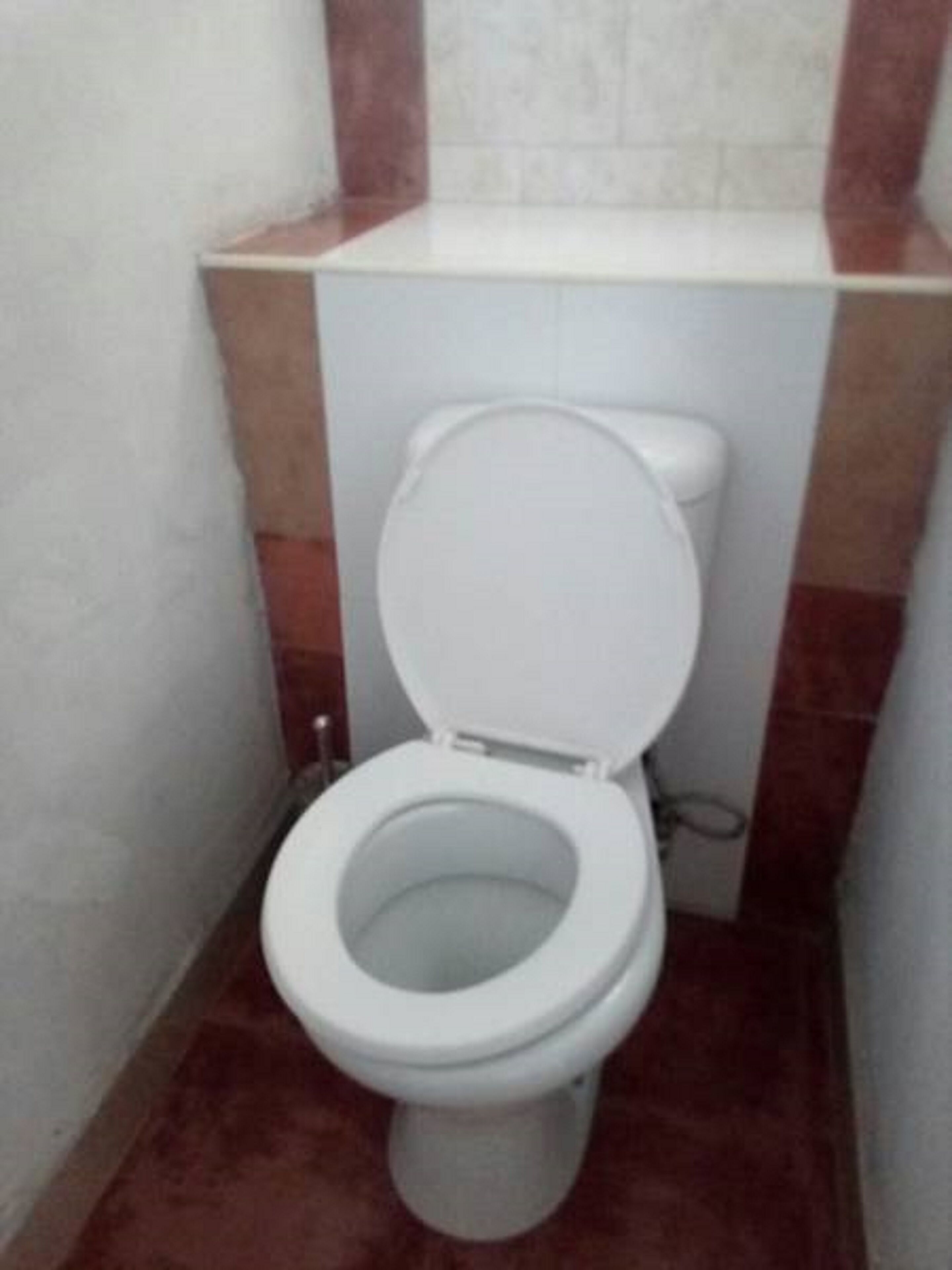 De petites toilettes blanches dans une salle de bain dont les murs sont recouverts de carreaux rouges et blancs.