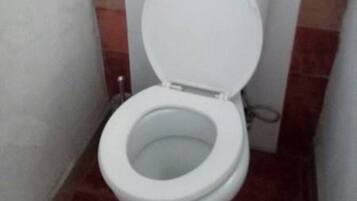 De petites toilettes blanches dans une salle de bain dont les murs sont recouverts de carreaux rouges et blancs.