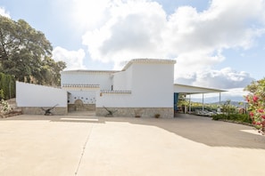 Un edificio moderno con base de piedra y paredes blancas, una entrada cubierta y un estacionamiento.