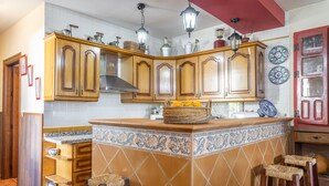 A kitchen with wooden cabinets, a tiled backsplash, hanging lights, and a fruit basket on the counter. - Holiday Home "Cortijo Rural Puerto Nuevo" with Pool, Garden, Terrace & Wi-Fi (Málaga)
