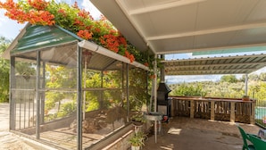 A covered patio with a grill, a green chair, a table, a birdcage, and potted plants. - Holiday Home "Cortijo Rural Puerto Nuevo" with Pool, Garden, Terrace & Wi-Fi (Málaga)