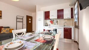 A modern kitchen with white and red cabinets, a dining table set with plates and cutlery, and a glass-top table. - Great Location with Charming Patio - Prato Verde - Girasole (San Felice del Benaco)