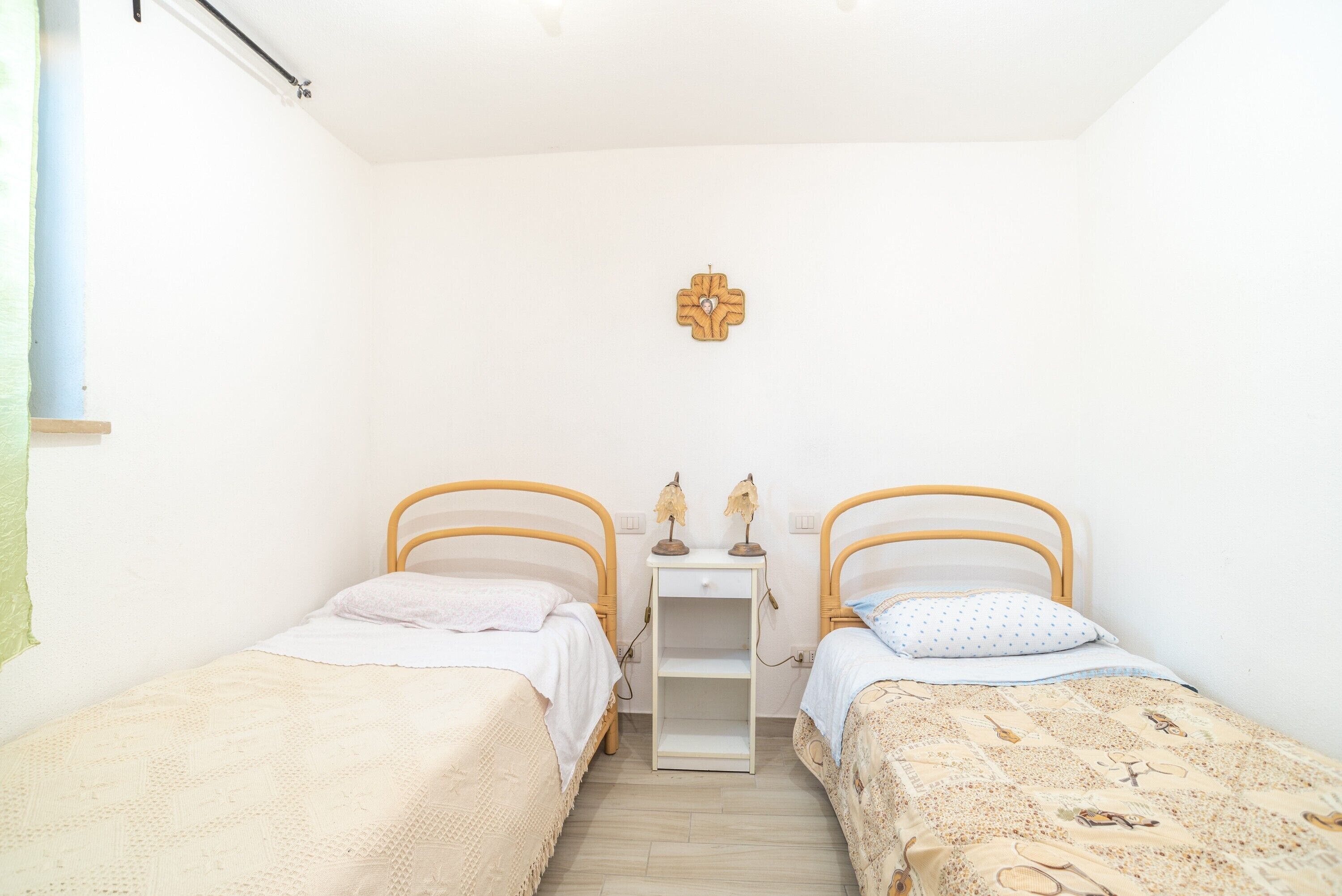 Een kleine, schone kamer met twee eenpersoonsbedden, een nachtkastje met een lamp en een decoratie aan de muur.