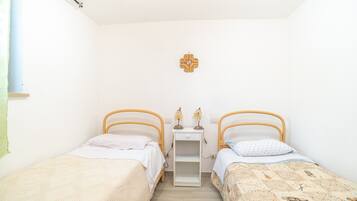 Een kleine, schone kamer met twee eenpersoonsbedden, een nachtkastje met een lamp en een decoratie aan de muur.