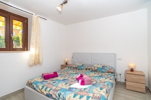 A bedroom with a bed, two bedside tables, a window with curtains, and a ceiling light.