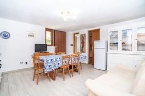 A dining area with a table and chairs, a television, a refrigerator, and a cabinet with glass doors.