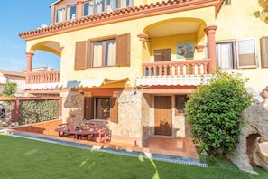 A two-story house with a balcony, a stone wall, and a small patio area.