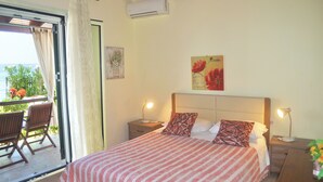 A bedroom with a bed, two bedside tables, a nightstand, a window with curtains, a chair, and a view of the outdoors. - Beachfront Holiday House Eftichia (Corfu)