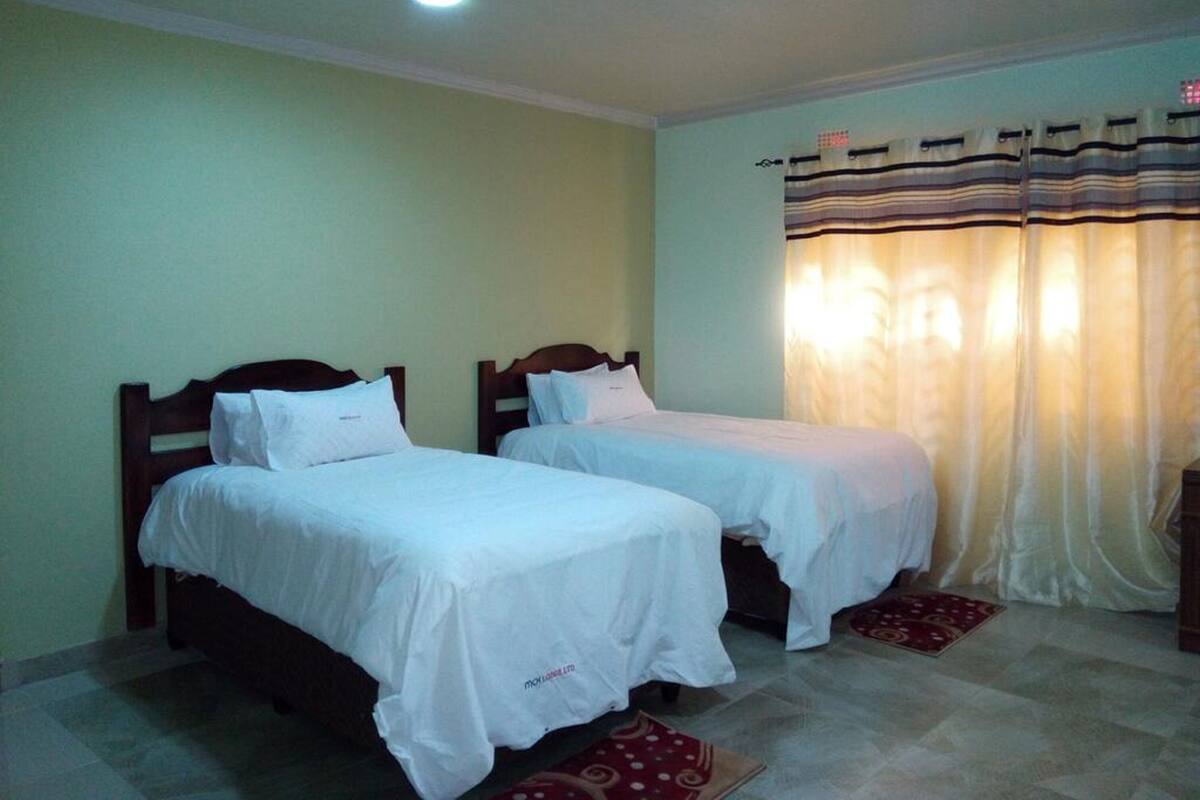 A room with two single beds, a small table, and a window with curtains.
