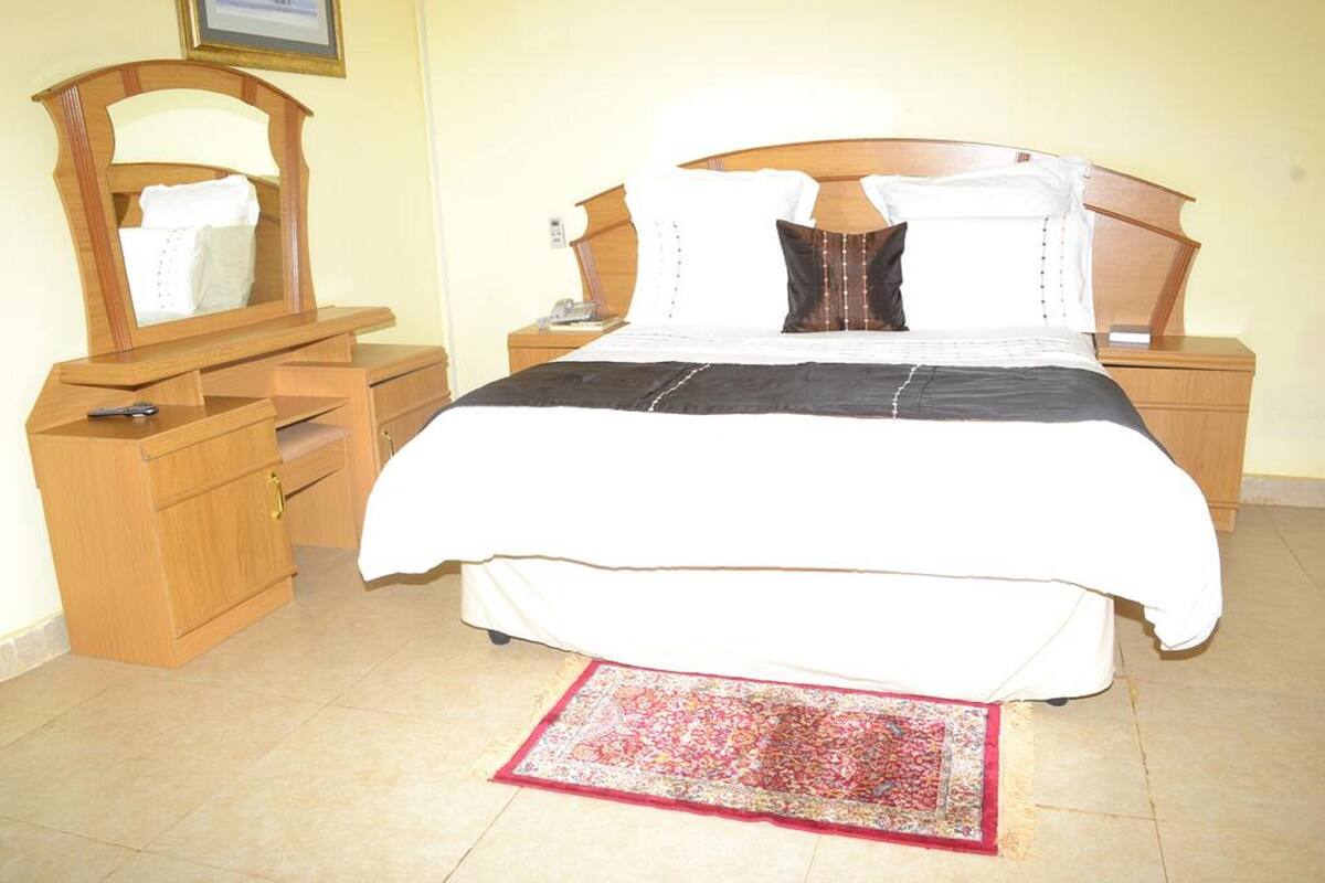 A bedroom with a wooden bed frame, a nightstand with a lamp, a dresser, and a mirror.