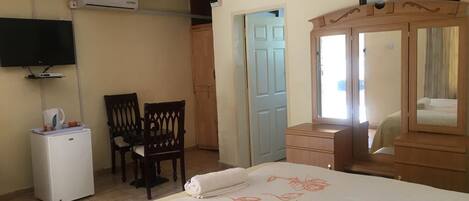 A bedroom with a bed, a dresser, a television, a desk, and a chair.