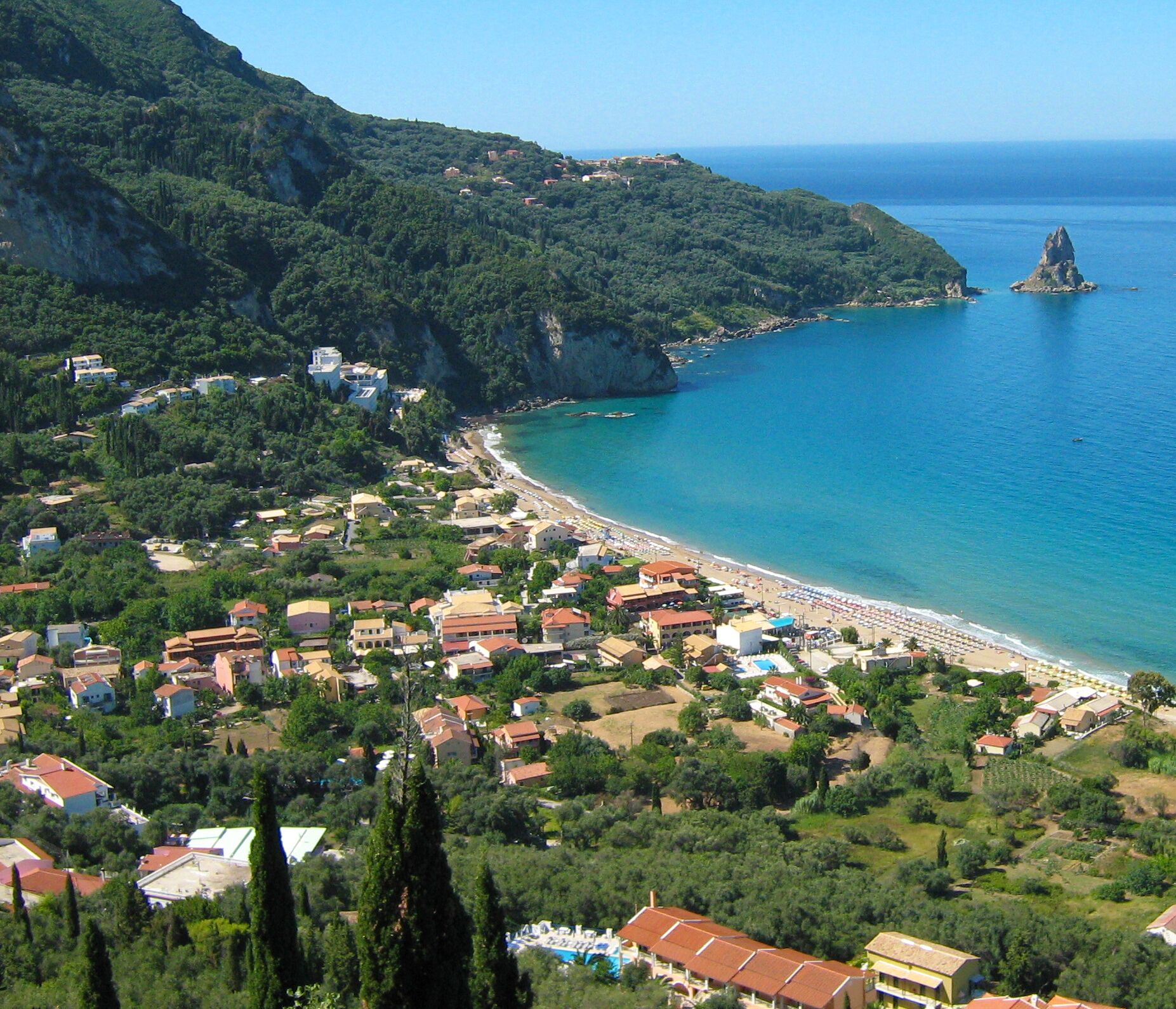 A coastal town with a beach, houses, and a prominent rock formation.