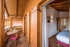 A wooden cabin with a balcony, a dining table with chairs, a bed, and a window with a view.