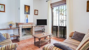 A living room with a brick fireplace, a television, striped sofas, and a balcony with a lattice door.