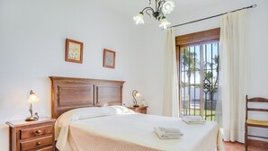 A bedroom with a bed, nightstand, lamp, and a view of the outdoors.