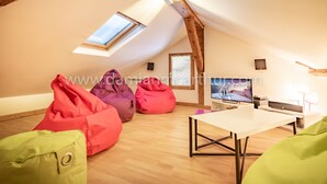 An attic room with a sloped ceiling, wooden beams, a skylight, a flat-screen TV, a table, and colorful bean bags.
