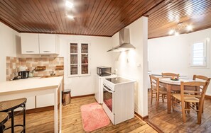 Uma cozinha compacta com armários brancos, forno embutido e uma área de refeições com cadeiras e mesa de madeira.