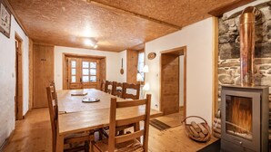 A wooden dining table with chairs, a stone wall, and a wood-burning stove.