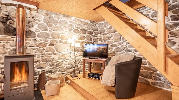 A cozy room with a stone wall, a fireplace, a television, and a wooden staircase.