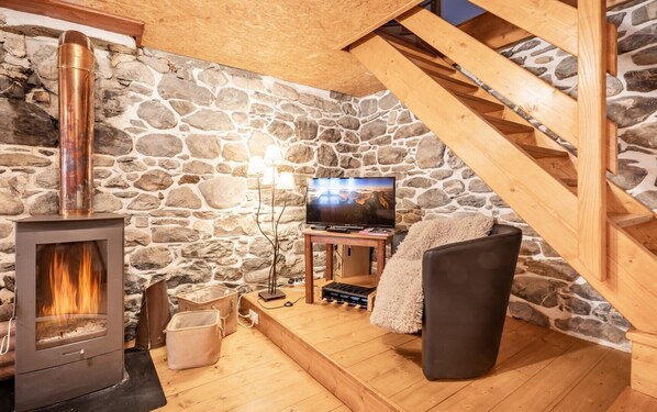 Um quarto acolhedor com parede de pedra, lareira, televisão e escada de madeira.