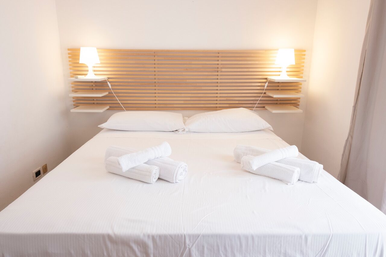 Una cama bien hecha con sábanas y almohadas blancas, dos lámparas de noche y un cabecero de madera.
