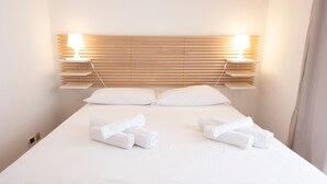 A neatly made bed with white linens and pillows, two bedside lamps, and a wooden headboard. - Villa Blumarine (San Vito Lo Capo)