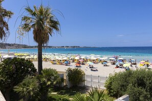 Een strand met veel parasols, mensen, palmbomen en een helderblauwe lucht.