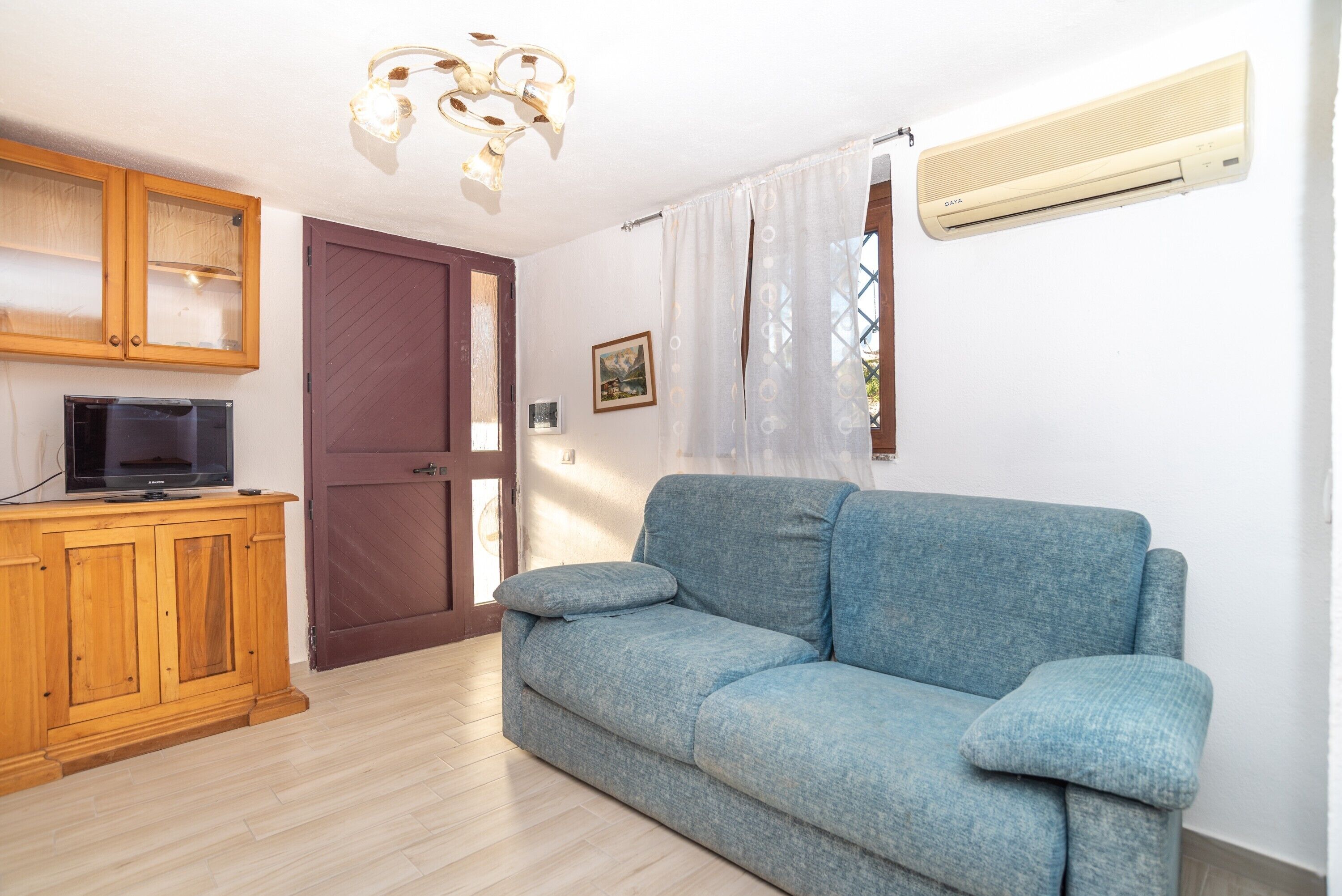 Een woonkamer met een bank, houten kast, televisie, airconditioning en een deur.