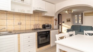 A kitchen with white cabinets, a brick backsplash, a gas stove, a built-in oven, and a dining area with a white table and chairs. - Centrally Located, Mediterranean Holiday Apartment with Garden and Terrace; Pets Allowed (san teodoro)