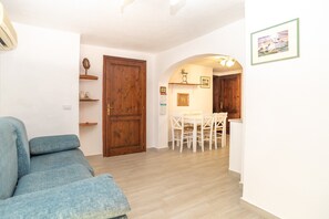 A living room with a blue sofa, a wooden door, and a dining area with white chairs and a table. - Centrally Located, Mediterranean Holiday Apartment with Garden and Terrace; Pets Allowed (san teodoro)