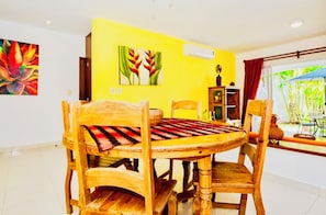 A dining area with wooden furniture, a yellow wall, and a window with a view of greenery.