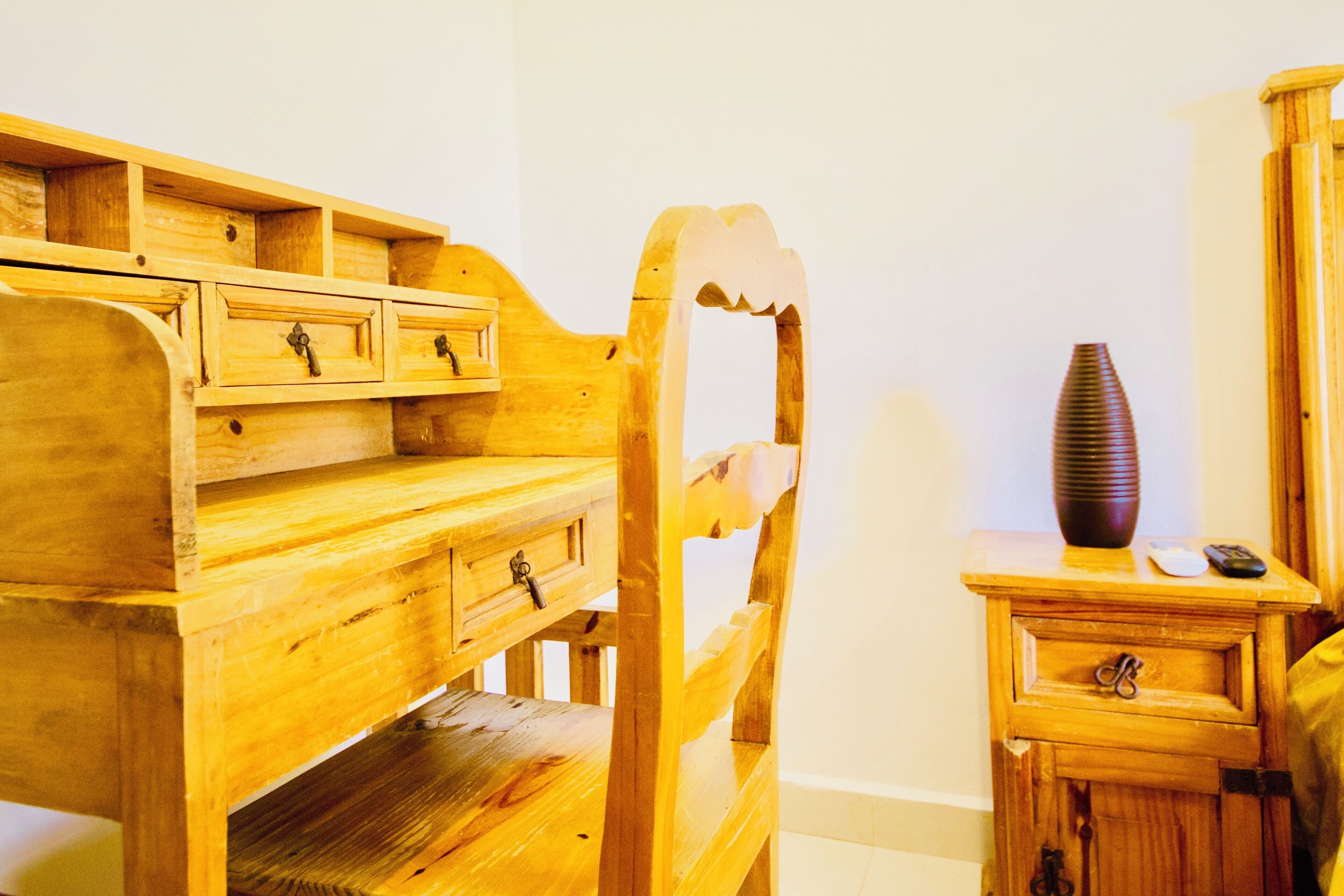 Una cama litera de madera con cajones, una mesita de noche pequeña y un florero.