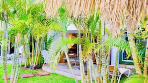 A lush garden with palm trees, a patio area with outdoor furniture, and a building with a green door. - Room-playacar - Deluxe Family Comfort Ba (Playa del Carmen)