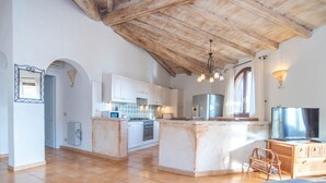 Une cuisine spacieuse avec un grand îlot central, des poutres apparentes en bois au plafond et un téléviseur.