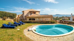Une piscine avec des chaises longues, une terrasse en pierre et une maison avec un toit en tuiles.